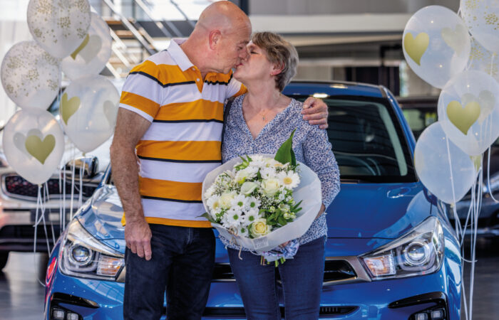 Un couple s'embrasse devant une voiture Kia bleu entourée de ballons