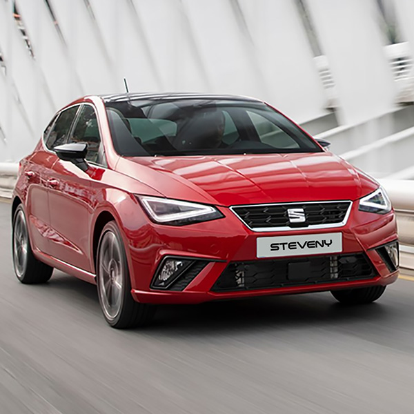 Une SEAT Ibiza rouge sur une route en ville avec une plaque Steveny