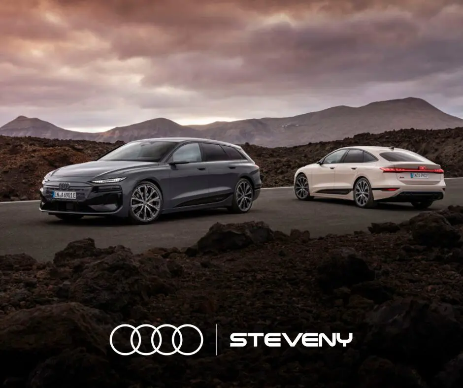 Deux Audi A6 e-tron 2025, l'une grise et l'autre blanche, stationnées sur une route entourée de rochers volcaniques sous un ciel nuageux.
