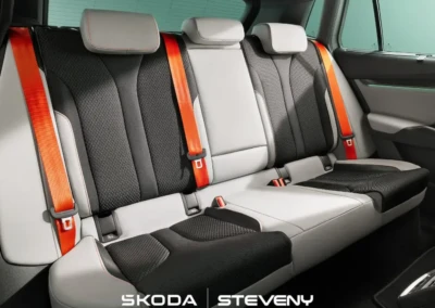 Banquette arrière de la Skoda Elroq avec sièges en tissu noir et gris, ceintures de sécurité oranges, dans l'habitacle lumineux.