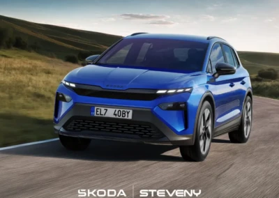 SUV Skoda Elroq bleu roulant sur une route, entouré de paysages verdoyants sous un ciel partiellement nuageux.