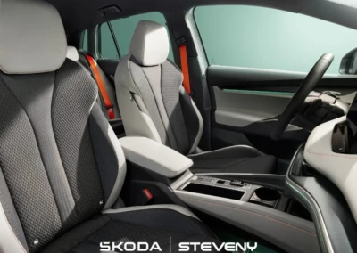 Intérieur de la Skoda Elroq avec sièges en tissu gris et blanc, ceintures de sécurité orange et tableau de bord moderne.
