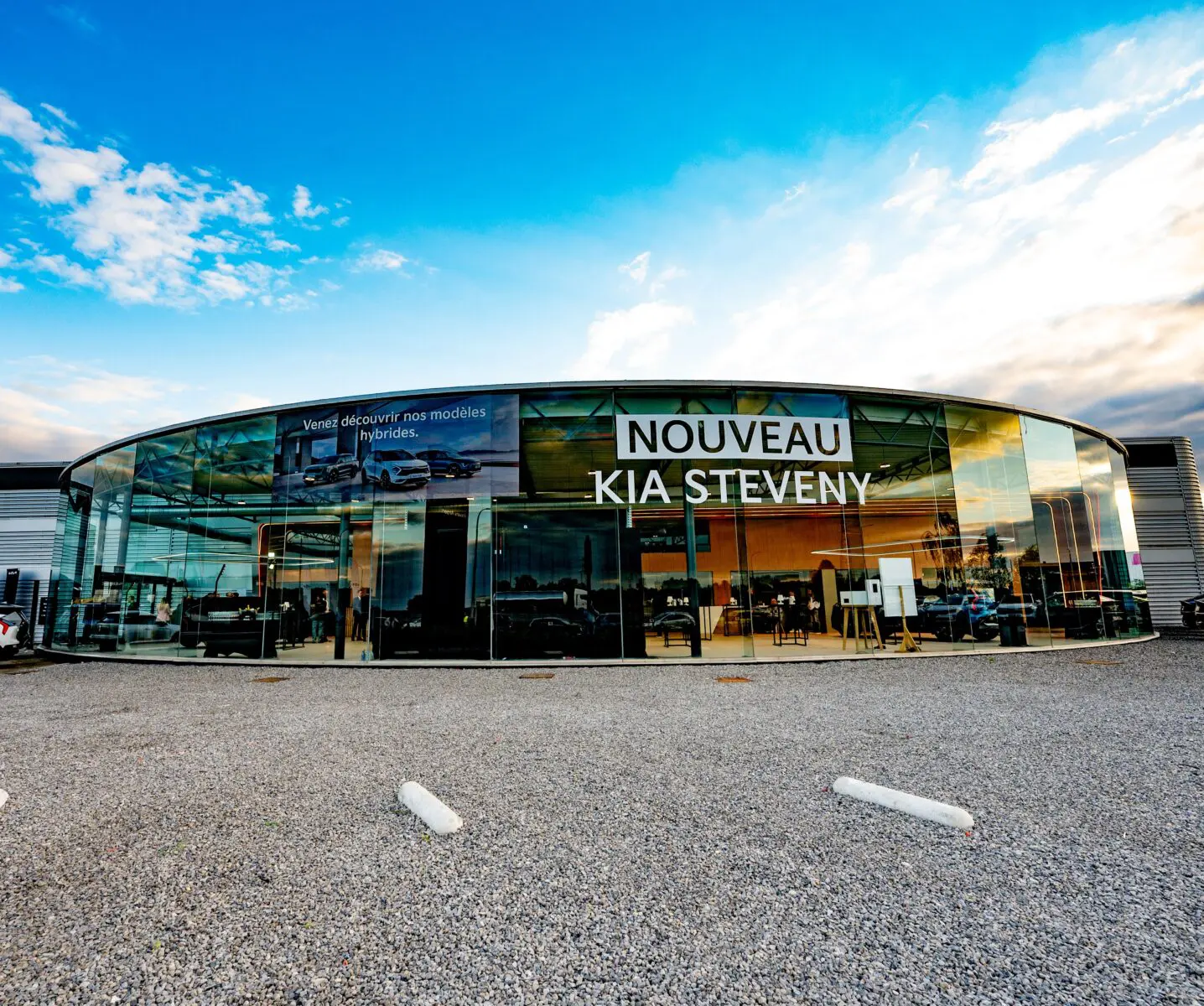 DSC_4124-min Façade vitrée de la concession Kia Steveny sous un ciel bleu avec des nuages.