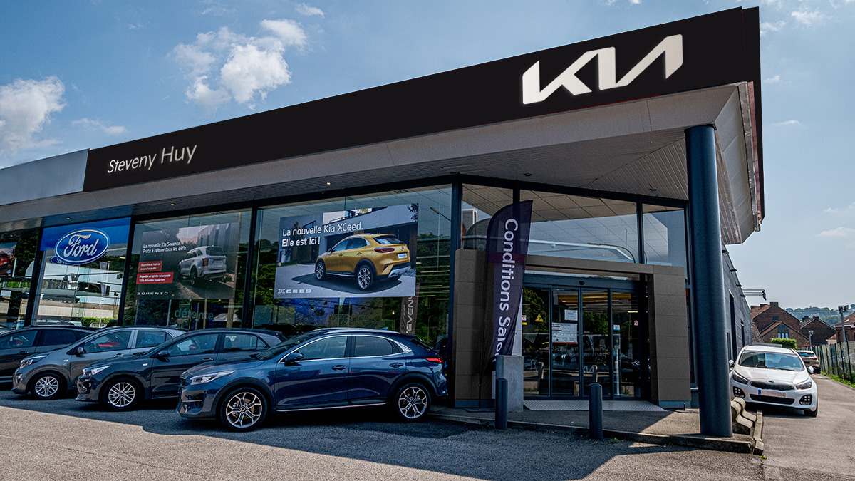 Concession Steveny à Huy avec panneaux Kia et Ford, plusieurs voitures garées devant, dont une Kia XCeed bleue.