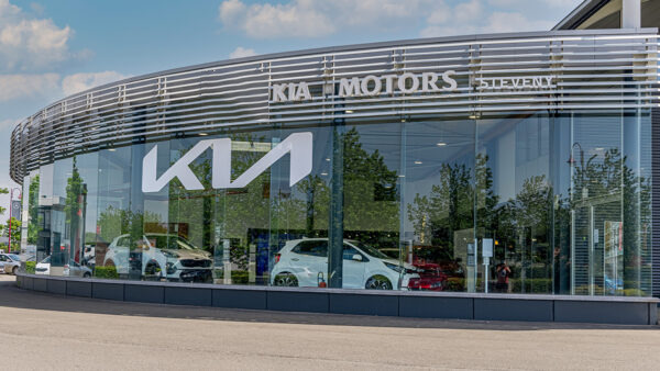 Concession Steveny Kia avec façade vitrée, deux voitures blanches visibles à l'intérieur, logo Kia sur la vitre.