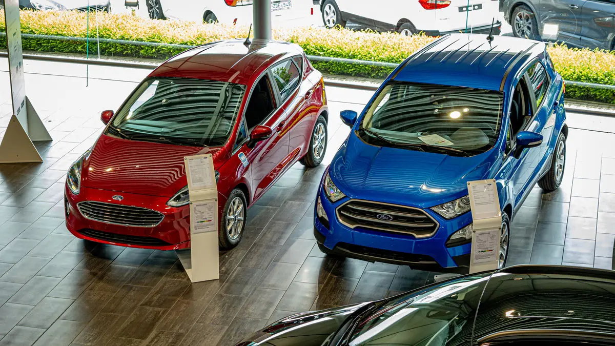 Deux voitures Ford, une rouge et une bleue, sont exposées dans une concession avec des fiches descriptives devant elles.