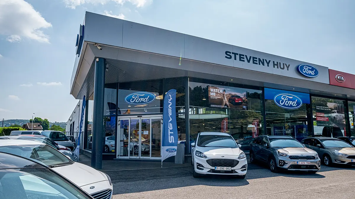 Façade de la concession Steveny Huy avec des voitures Ford et Kia garées devant les vitrines.
