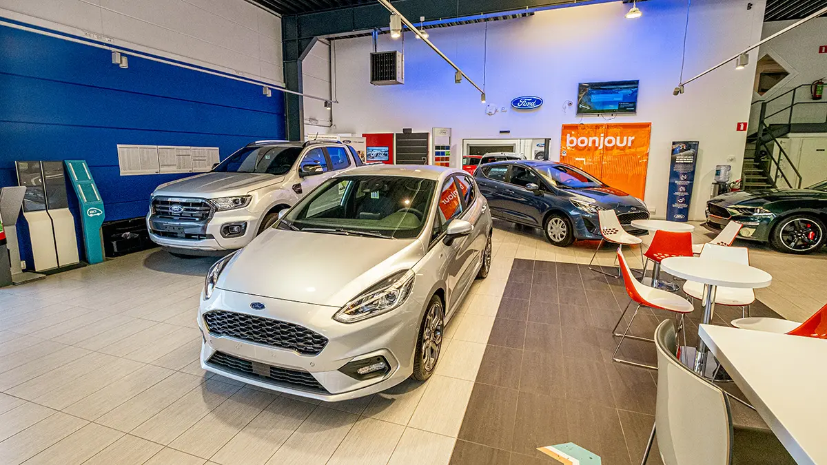 Salle d'exposition Ford avec une Ford Fiesta argentée au premier plan, entourée de divers modèles Ford dans un espace moderne.