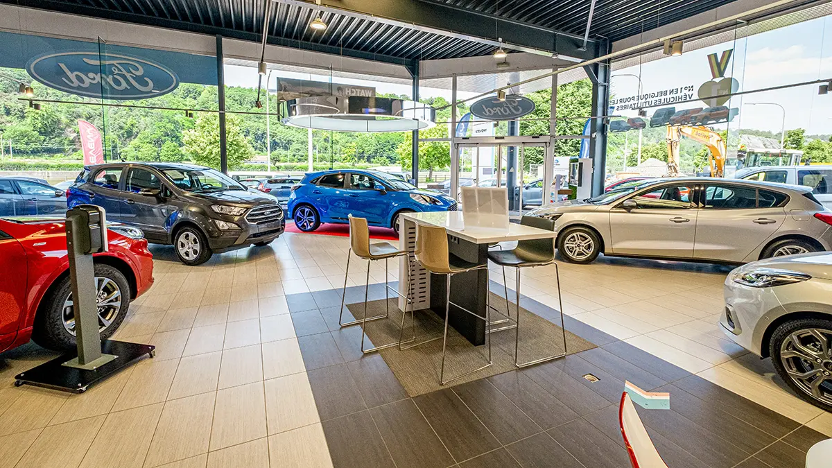 Voitures Ford exposées dans une concession avec intérieur moderne, grandes baies vitrées et vue sur l'extérieur verdoyant.