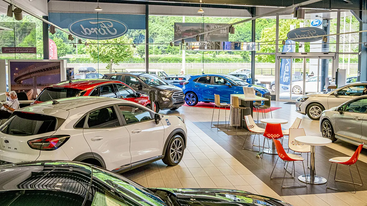 Intérieur d'une concession Ford à Huy avec plusieurs voitures exposées, dont un modèle blanc Puma et un modèle bleu.