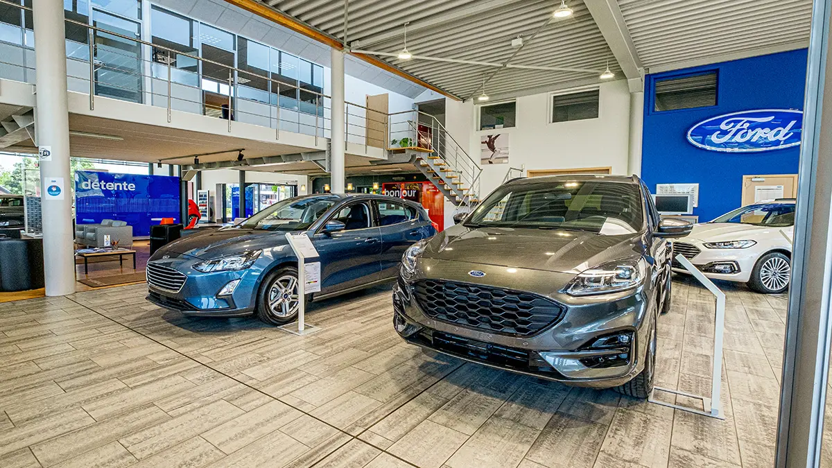 concession-ford-marche-3 Deux voitures Ford exposées dans une concession automobile moderne avec un logo Ford bleu au mur.