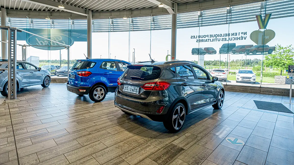 concession-ford-marche-4 Des voitures Ford grises et bleues exposées dans une concession avec de grandes fenêtres et un sol en carrelage.