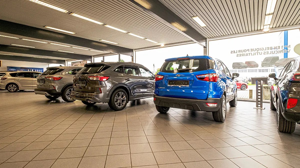 concession-ford-nivelles-5 Des voitures Ford grises et bleue sont exposées dans une concession automobile lumineuse avec un sol carrelé.