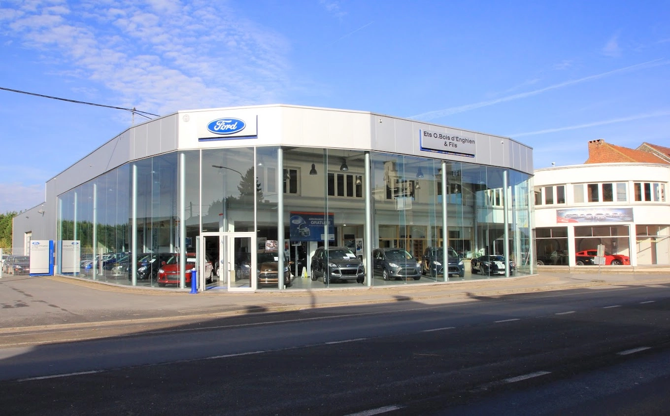 Concession Ford à Soignies avec façade vitrée et plusieurs voitures exposées à l'intérieur.
