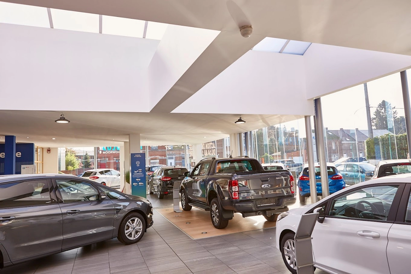 Intérieur d'une concession Ford avec plusieurs voitures exposées, dont un Ford Ranger gris au centre, éclairé par la lumière naturelle.