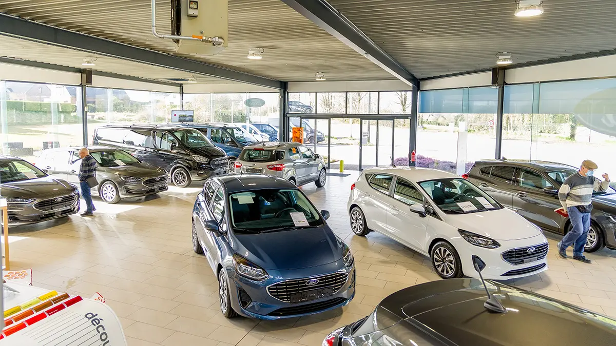 concession-ford-somzee-4 Intérieur lumineux d'une concession Ford avec plusieurs modèles de voitures exposés, incluant des Ford bleues et blanches.