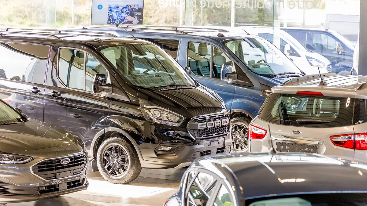 concession-ford-somzee-5 Véhicules Ford stationnés à l'intérieur d'une concession automobile, incluant un van noir et plusieurs voitures de différentes couleurs.