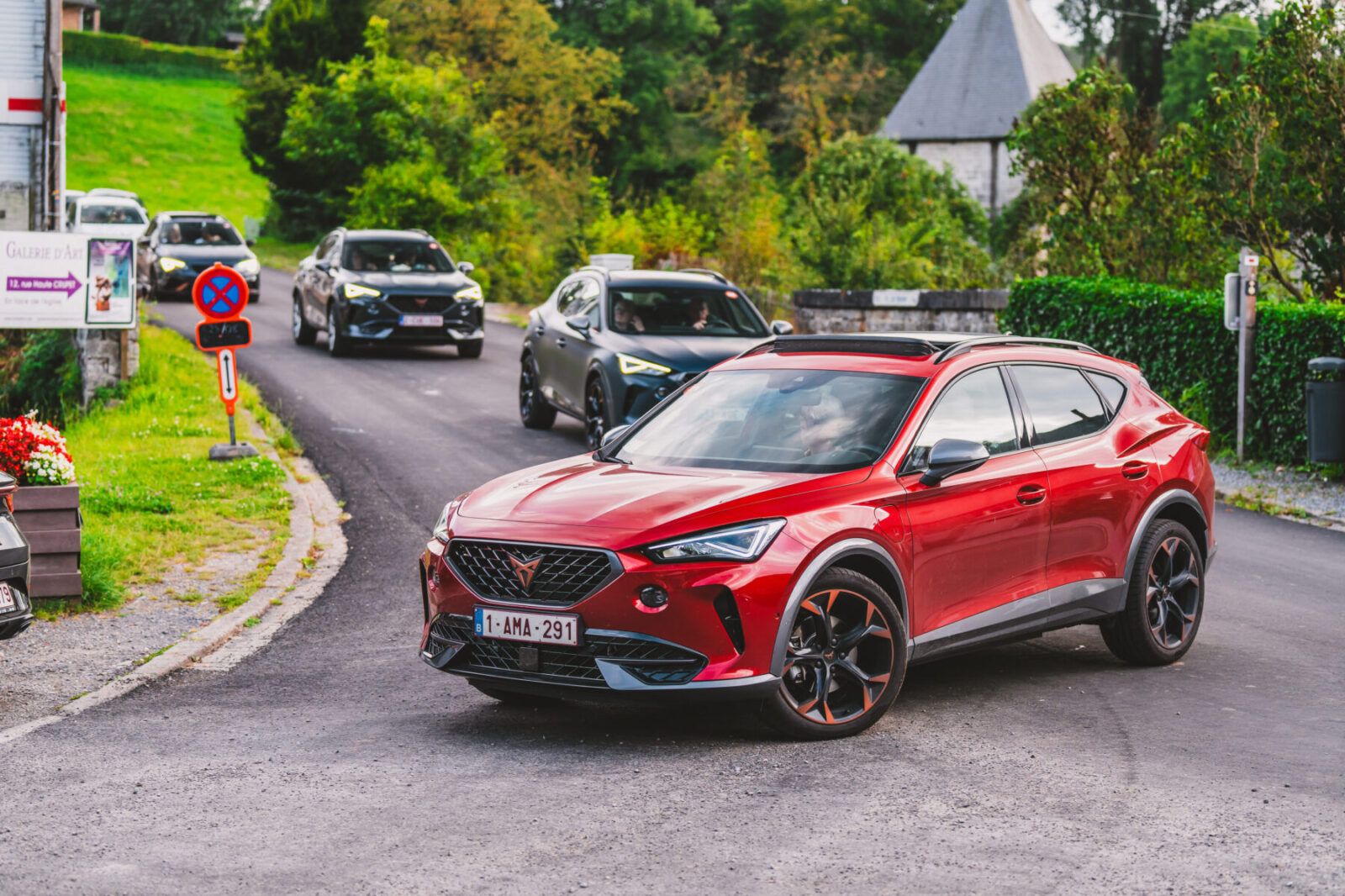 Voiture CUPRA rouge sur une route, entourée d'autres véhicules, avec un paysage verdoyant en arrière-plan.