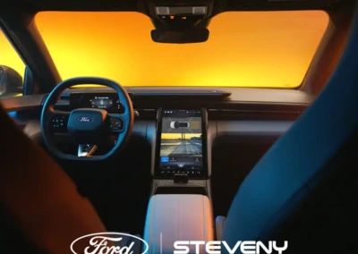 Intérieur d'une voiture Ford avec tableau de bord numérique et écran central, volant visible, fond jaune lumineux.