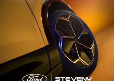 Roue d'une voiture Ford avec jante noire et argentée sur fond jaune-orange, logos Ford et Steveny visibles.