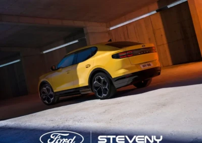 Voiture Ford jaune stationnée dans un parking en béton avec le logo Steveny visible en bas de l'image.
