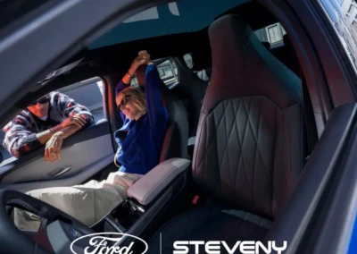 Deux personnes discutent à travers la fenêtre ouverte d'une voiture Ford avec un intérieur en cuir noir.