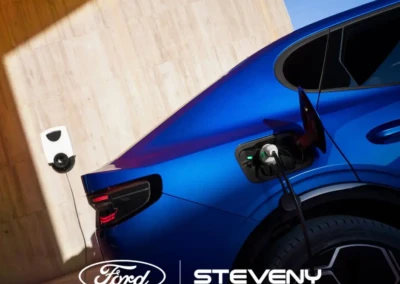 Voiture Ford bleue en train de se recharger sur une borne murale blanche, logo Steveny visible.