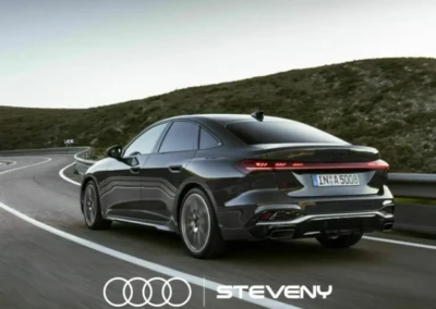 Audi A5 Sedan noire en conduite sur une route sinueuse, avec un logo Steveny en bas.