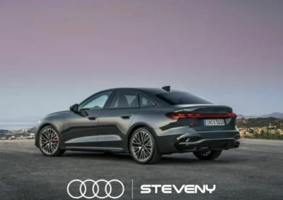 Audi A5 Sedan grise stationnée sur une route avec un ciel rose en arrière-plan, logo Steveny visible en bas.