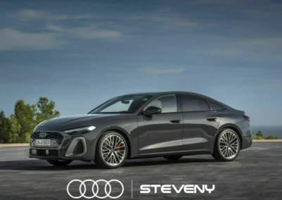 Audi A5 Sedan grise stationnée sur une route, avec un ciel bleu en arrière-plan et le logo Steveny visible devant.