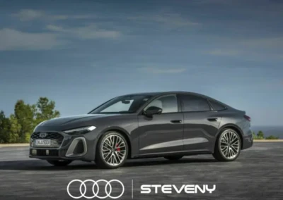 Audi A5 Sedan grise stationnée sur une route dégagée, ciel bleu en arrière-plan, logo Steveny visible.