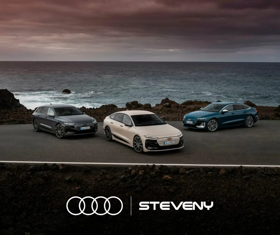 Trois Audi A6 e-tron 2025 de différentes couleurs sont garées sur une route côtière sous un ciel nuageux.