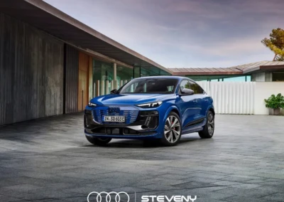 Voiture Audi Q6 Sportback e-tron bleue stationnée devant un bâtiment moderne avec un ciel nuageux en arrière-plan.