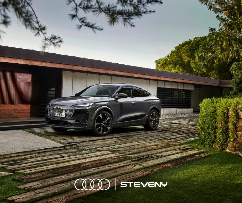 Voiture Audi Q6 Sportback e-tron grise stationnée devant une maison moderne, entourée de verdure et d'arbres.