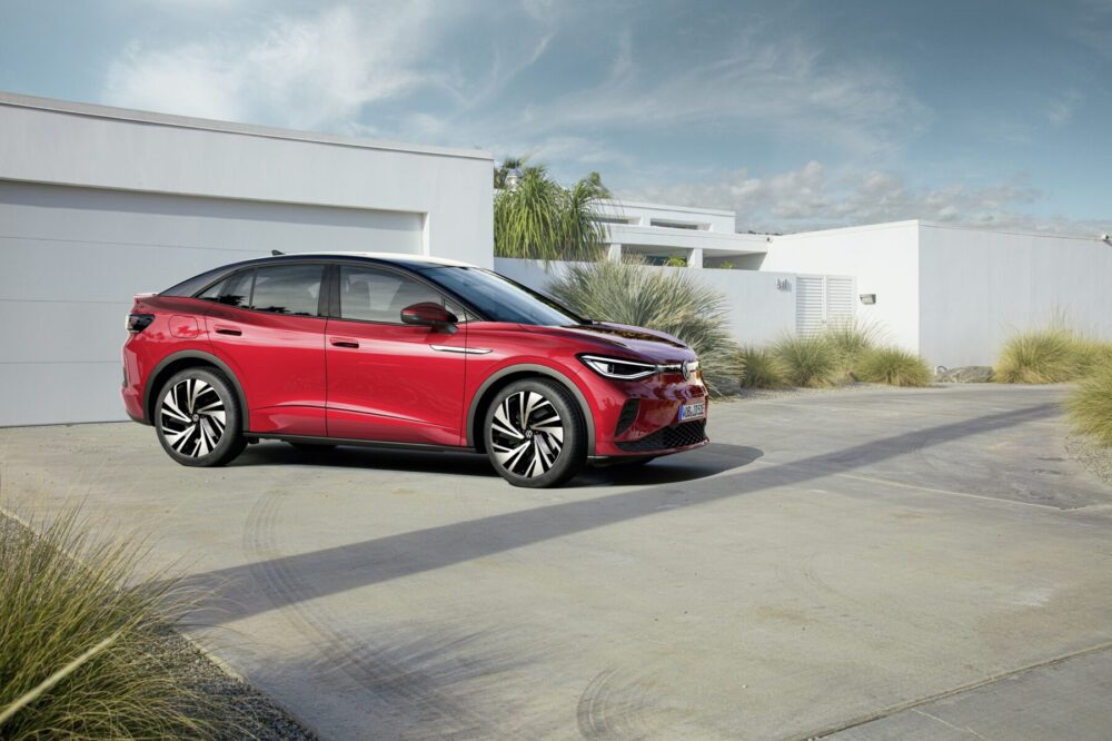 Voiture rouge Volkswagen ID.5 garée devant une maison moderne, entourée de végétation et sous un ciel partiellement nuageux.
