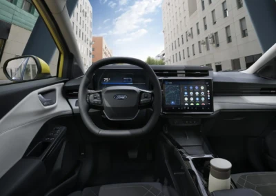 Intérieur d'une Ford Puma 2024 avec volant, tableau de bord numérique et écran tactile affichant des applications, vue sur des bâtiments urbains.