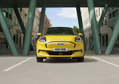 Voiture Ford Puma 2024 jaune stationnée sous une structure moderne avec des piliers verts, entourée de bâtiments urbains.