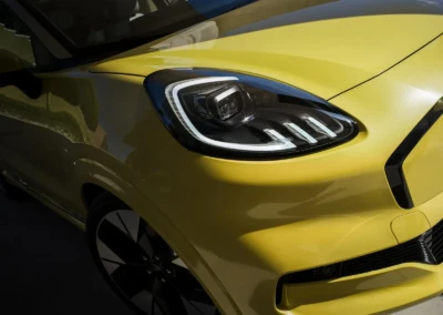 Avant de vous donner le texte alt, je vous rappelle qu'il est important de s'assurer que l'image est bien accessible, car le lien que vous avez partagé semble être incorrect. Texte alt : "Vue rapprochée de l'avant d'une Ford Puma 2024 jaune, montrant le phare et la calandre."