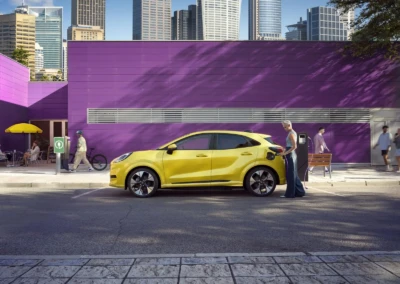 Voiture Ford Puma 2024 jaune stationnée devant un mur violet, avec une personne en train de la recharger.