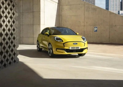 Voiture Ford Puma 2024 jaune stationnée dans un parking en béton, avec bâtiments en arrière-plan.