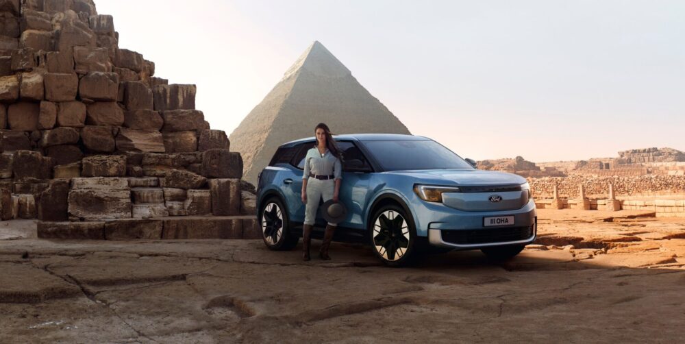 Un Ford Explorer bleu est garé devant une pyramide, avec une personne debout à côté sur un sol en pierre.