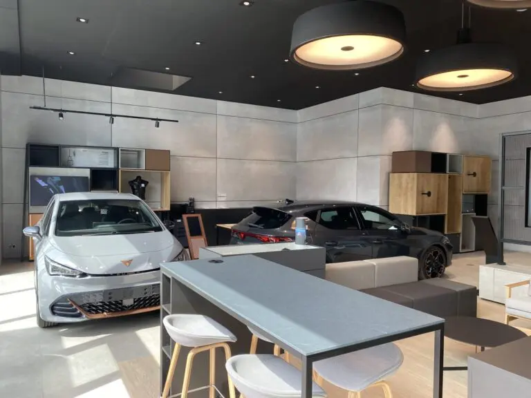 Deux voitures CUPRA grises sont exposées dans un showroom moderne avec des meubles en bois et des luminaires suspendus.