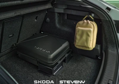 Coffre d'une Skoda Enyaq 2025 avec une valise noire et un sac à dos beige suspendu sur le côté.