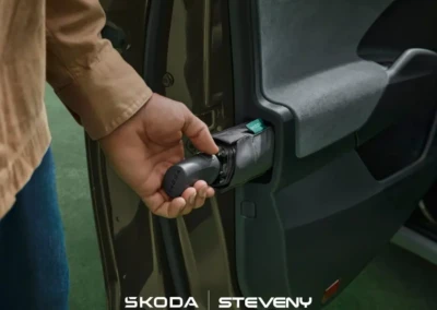 Main tenant un parapluie Skoda dans une portière de voiture ouverte, avec intérieur gris et extérieur marron.