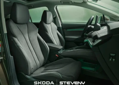 Intérieur de la Skoda Enyaq 2025 avec sièges avant en tissu gris et volant visible, éclairage intérieur vert.