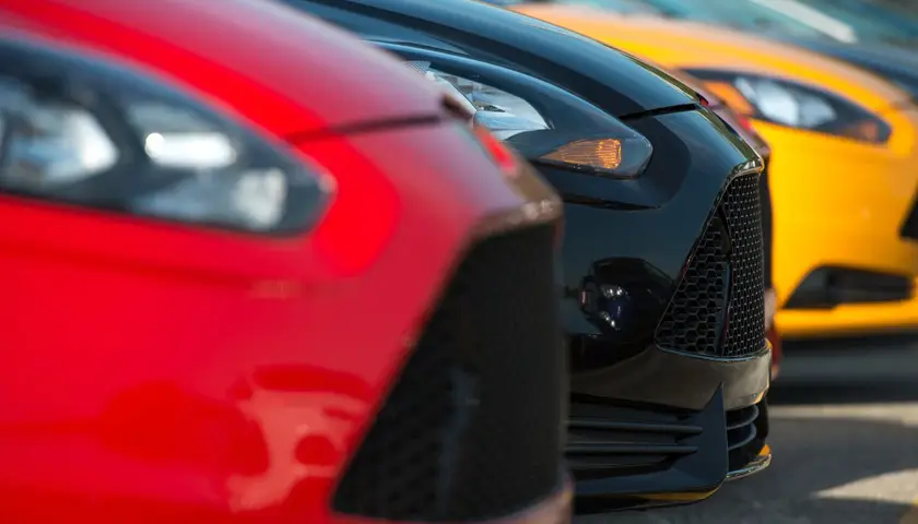 Des voitures alignées avec des carrosseries rouges, noires et jaunes, vues de l'avant, sur un parking ensoleillé.