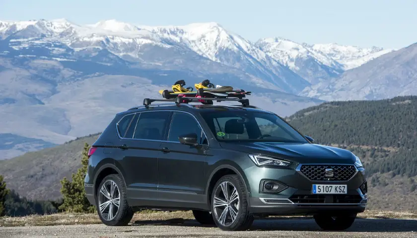 SUV SEAT avec skis sur le toit, stationné devant un paysage de montagnes enneigées sous un ciel bleu.