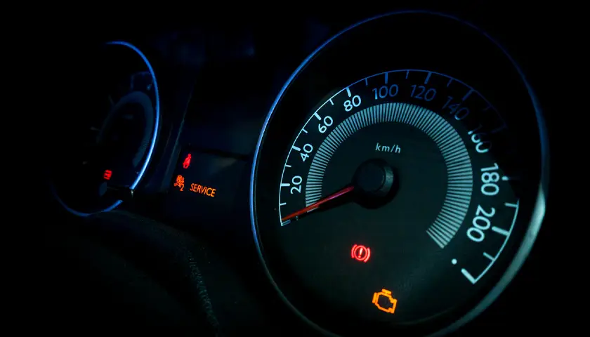Tableau de bord de voiture affichant un compteur de vitesse illuminé en bleu et orange, avec des voyants d'avertissement allumés.