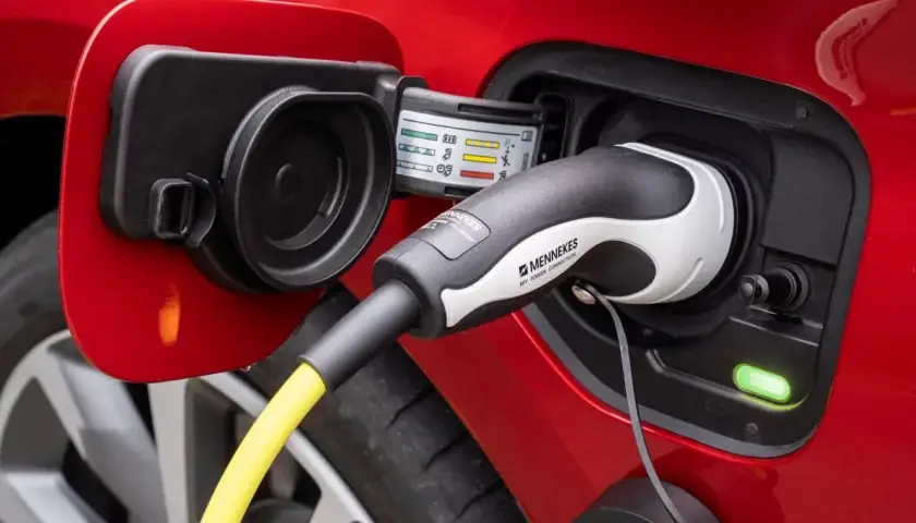Prise de recharge d'une voiture hybride rouge, connectée avec un câble de charge jaune et un indicateur lumineux vert allumé.