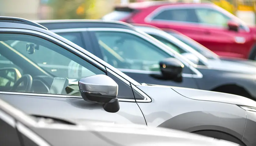 Voitures de différentes couleurs alignées sur un parking, vue de profil avec focus sur les rétroviseurs et fenêtres latérales.